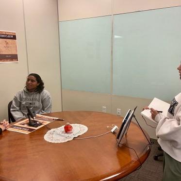 two women are sitting and talking where one lady is looking at them 