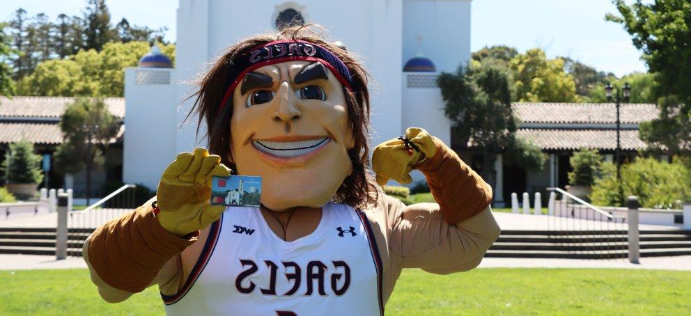 Gideon the mascot holding a credit card in front of the Saint Mary's College Chapel